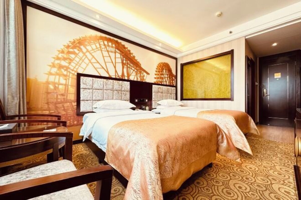 A hotel room with two beds, a large window with a view of a Ferris wheel, a wooden desk, and a large mirror.