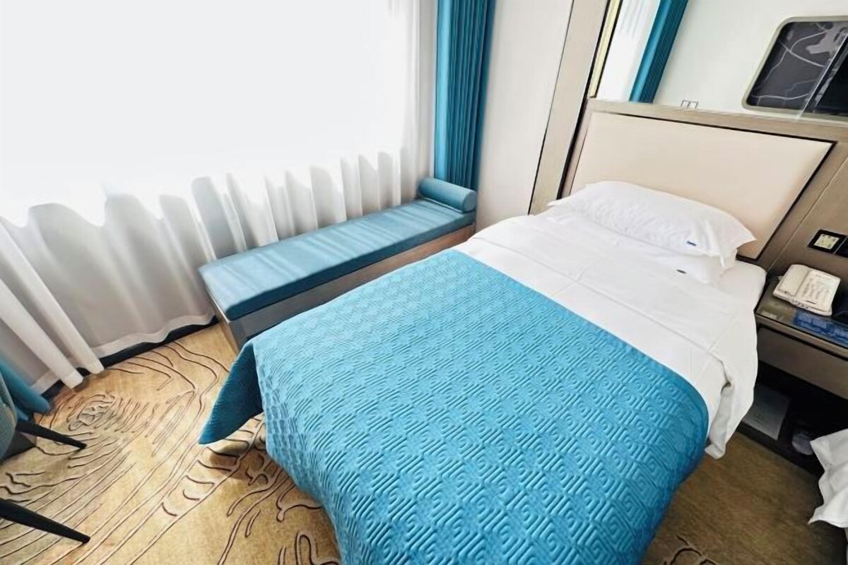 Une chambre d’hôtel avec un lit, une banquette, une table de chevet et une fenêtre avec des rideaux.