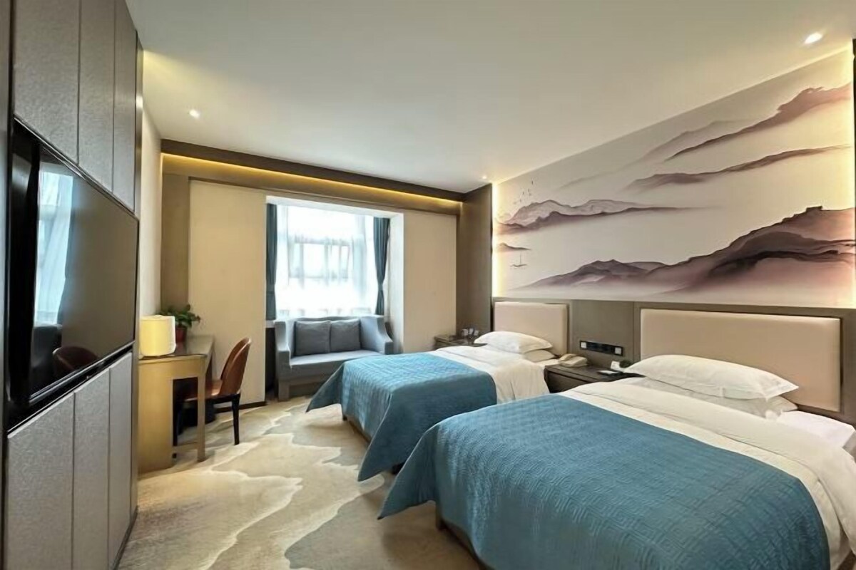 Une chambre d’hôtel avec deux lits, un bureau, une chaise, une télévision et un grand tableau au mur.