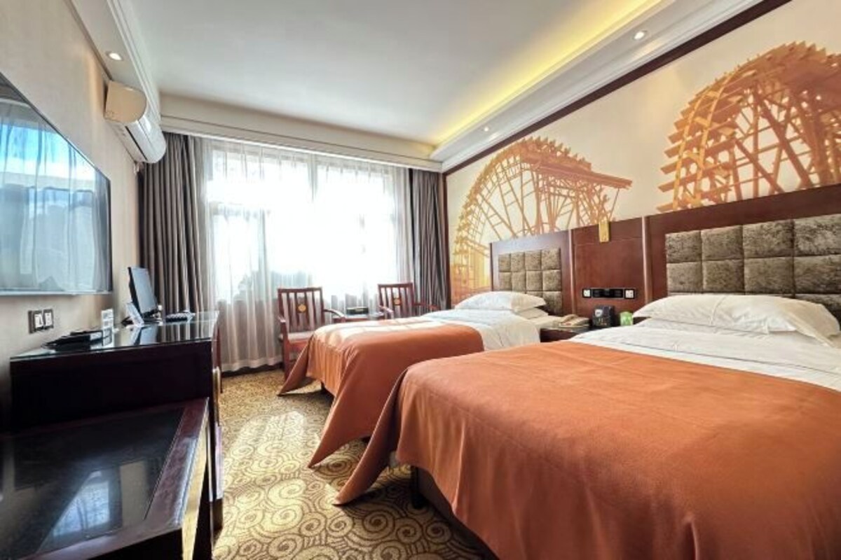 A hotel room with two beds, a desk, a chair, and a large window with curtains.
