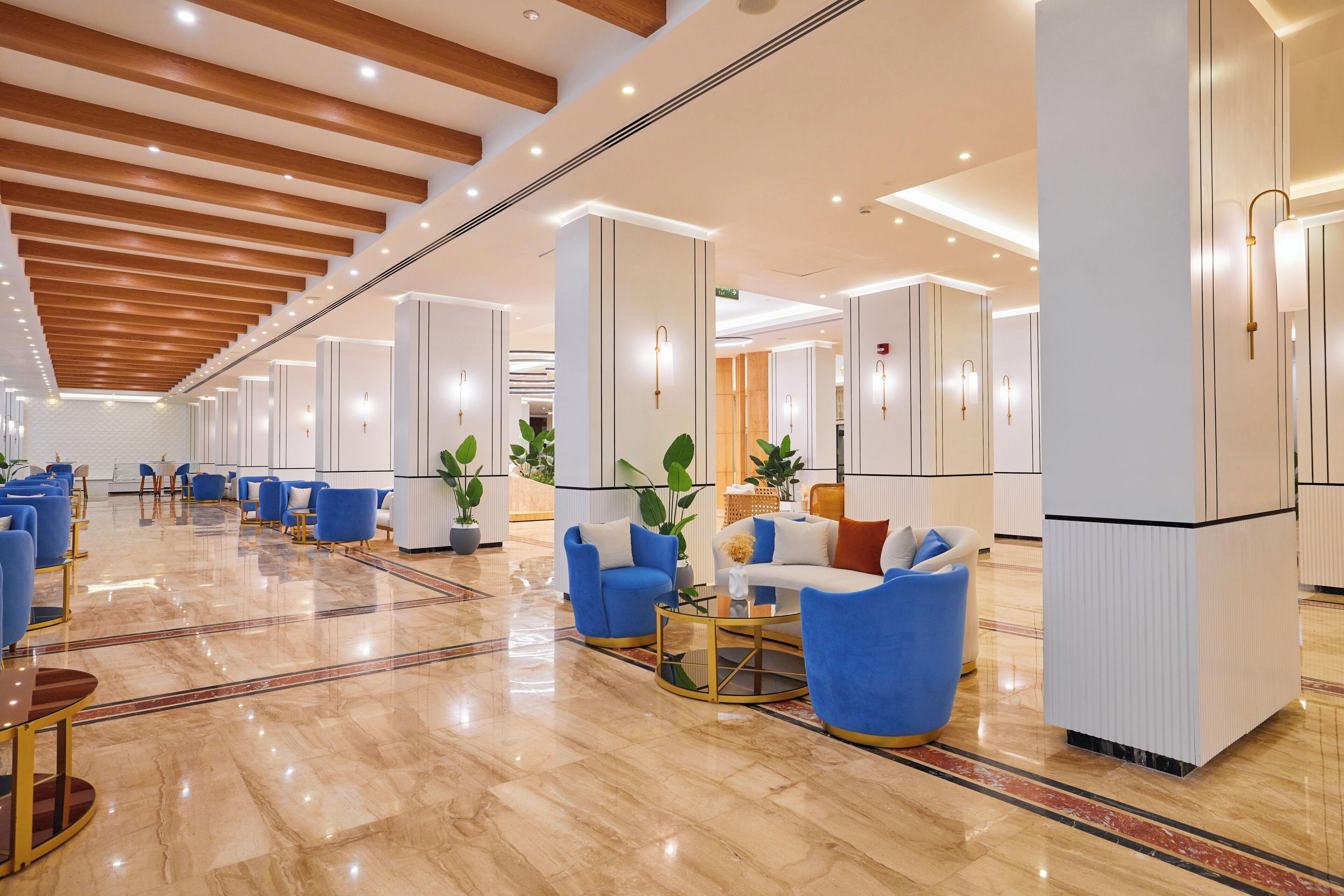 A spacious lobby with a polished marble floor, blue seating, and a high ceiling with wooden beams.