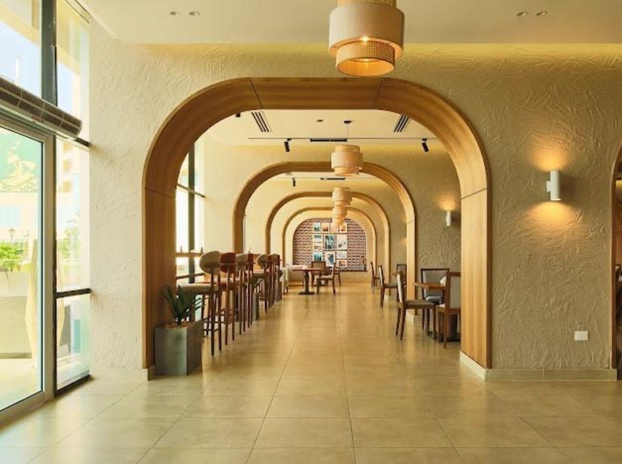 A corridor with arched ceilings, tables, chairs, and a view of a brick wall with framed pictures.