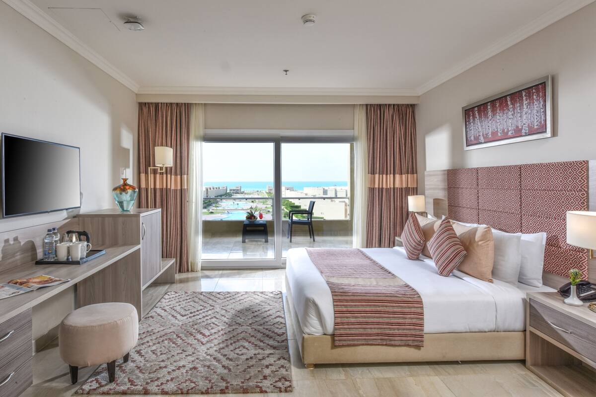 Une chambre d’hôtel avec un lit, une table de chevet, une télévision, un bureau et une vue sur la mer.