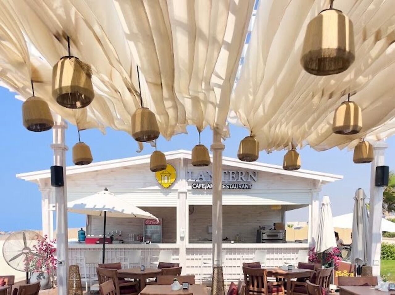 A restaurant with outdoor seating, white canopies, and hanging light fixtures.