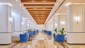 Een hotel lobby met een lange gang, blauwe stoelen, witte banken en houten balken in het plafond.
