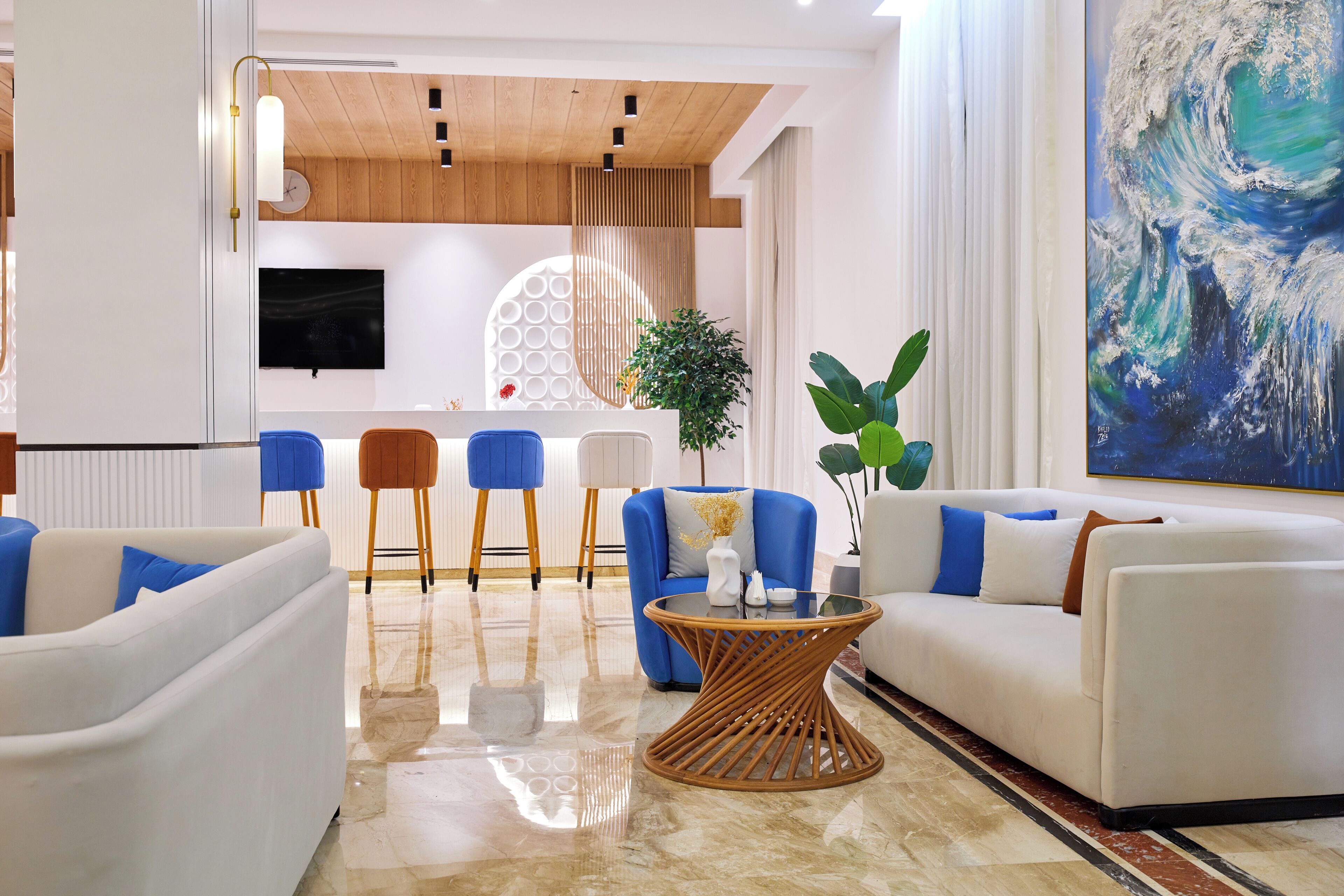 A modern living room with a white sofa, blue chairs, a glass coffee table, and a large abstract painting.