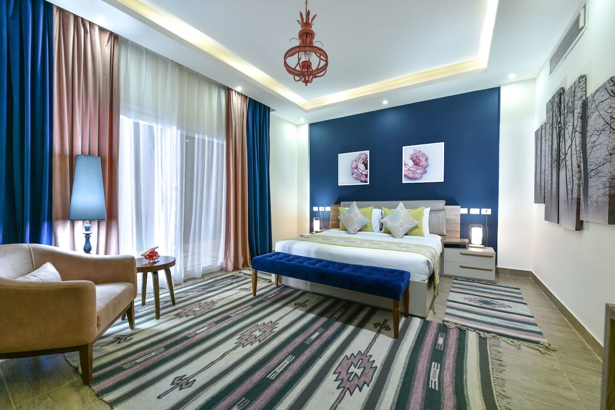 Une chambre d’hôtel comprenant un lit, un canapé, une table de chevet, une lampe, un lustre et des œuvres d’art accrochées aux murs.