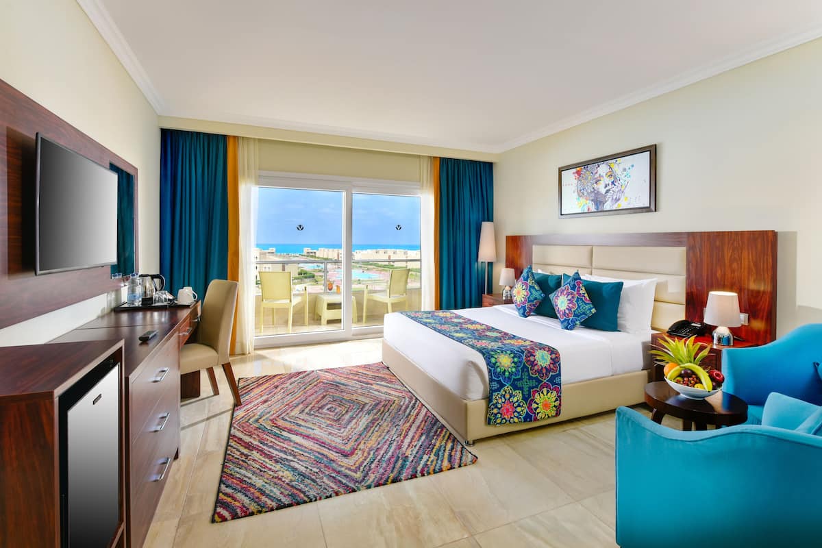 Une chambre d’hôtel comprenant un lit, un bureau, une chaise, une télévision et un balcon avec vue sur l’océan.