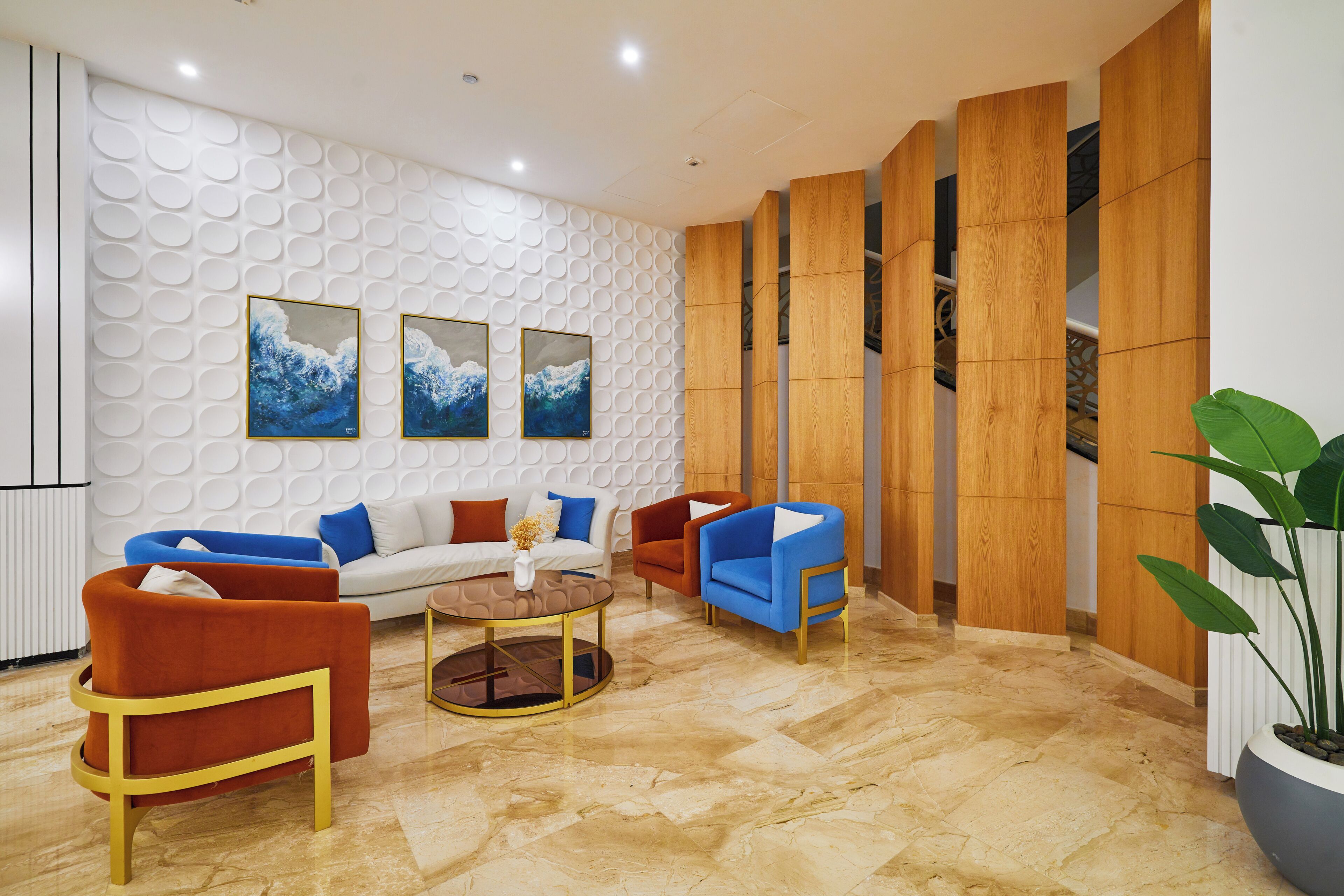 Un hall moderno con una pared blanca texturizada, un sofá, dos sillones, una mesita de centro y una planta en maceta.