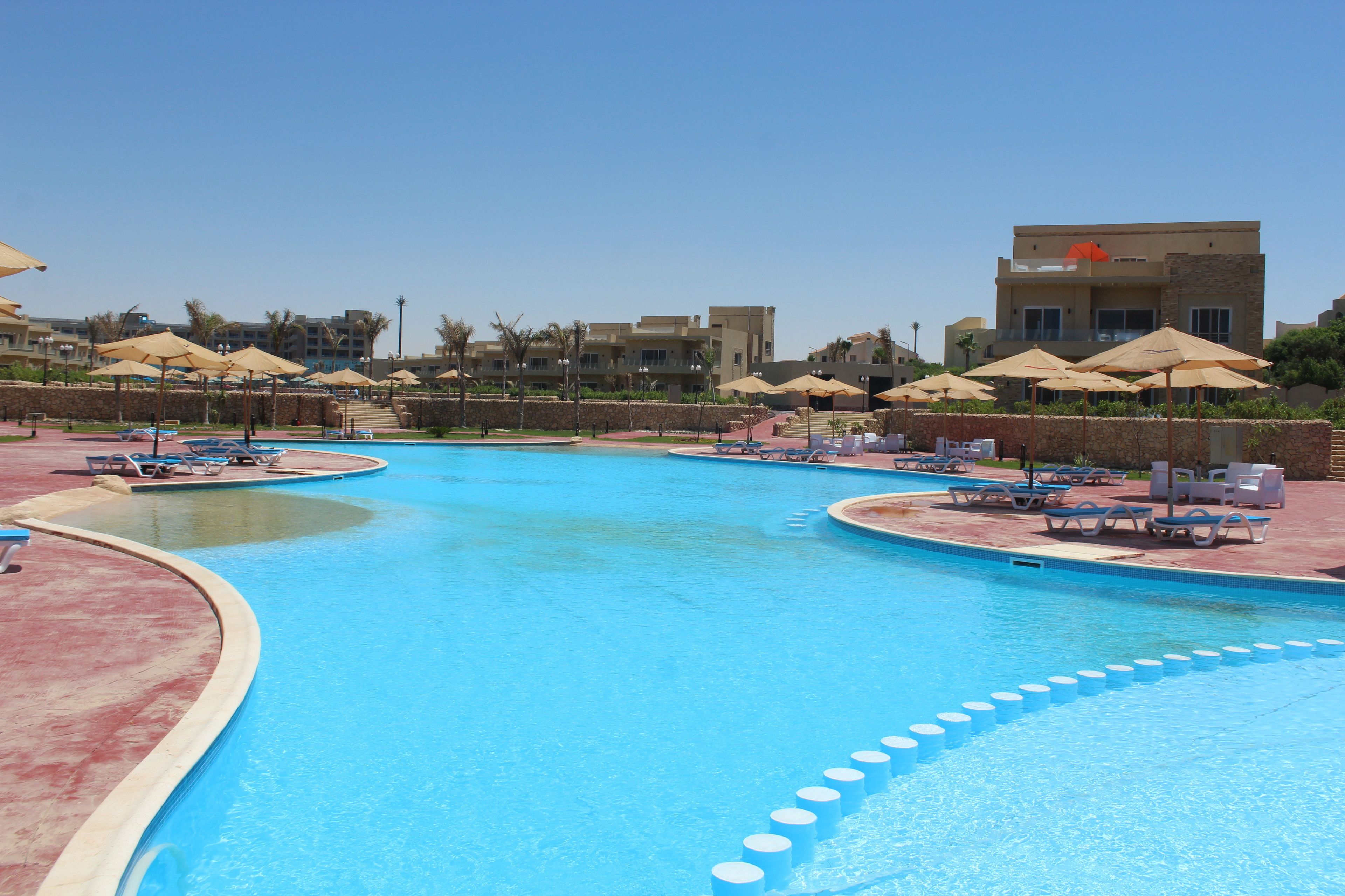 A swimming pool with multiple lanes, lounge chairs, and umbrellas.