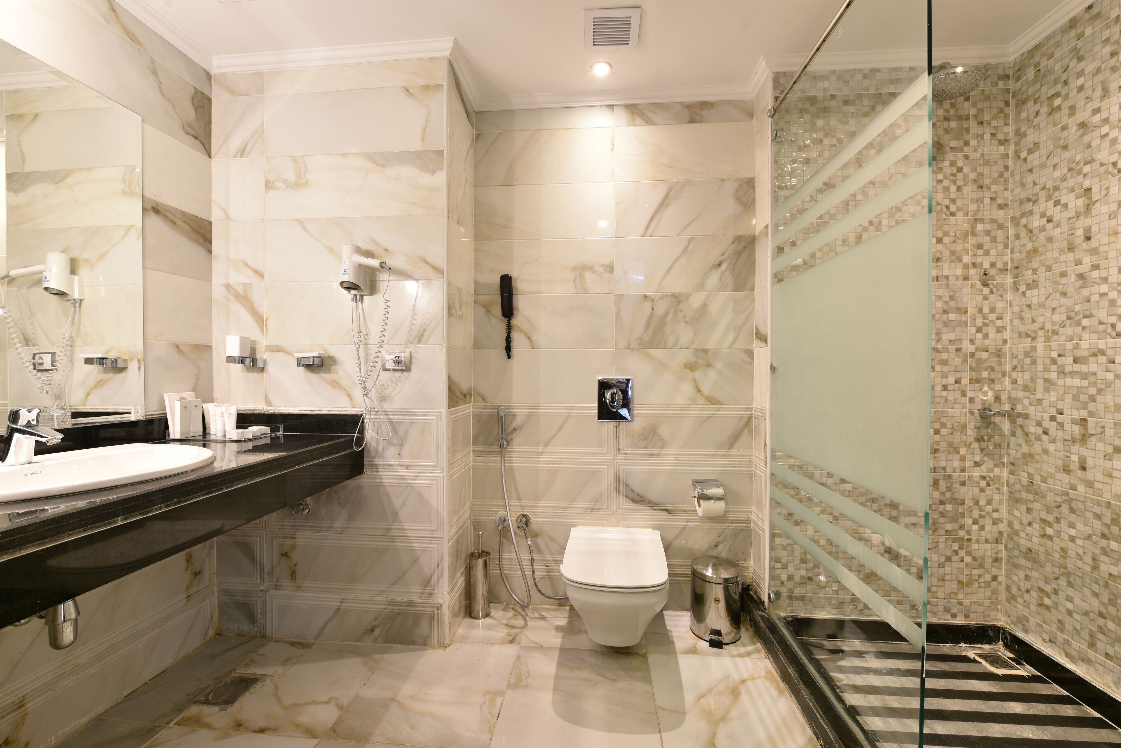 Un bany modern amb un lavabo de marbre, un vàter i una zona de banyera amb envàs de vidre.