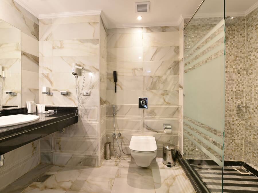 Un bany modern amb un lavabo de marbre, un vàter i una zona de banyera amb envàs de vidre.