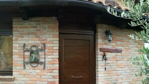 Un bâtiment en briques avec une porte en bois, une petite enseigne au-dessus de la porte et deux plantes en pot de chaque côté.