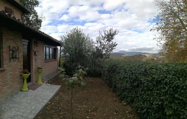 A brick house with a small garden, a potted plant, and a view of hills in the background. - Il Castagneto (Camerino)