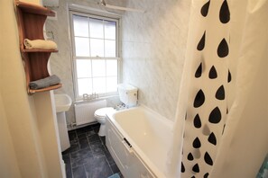 A bathroom with a bathtub, toilet, and a window.