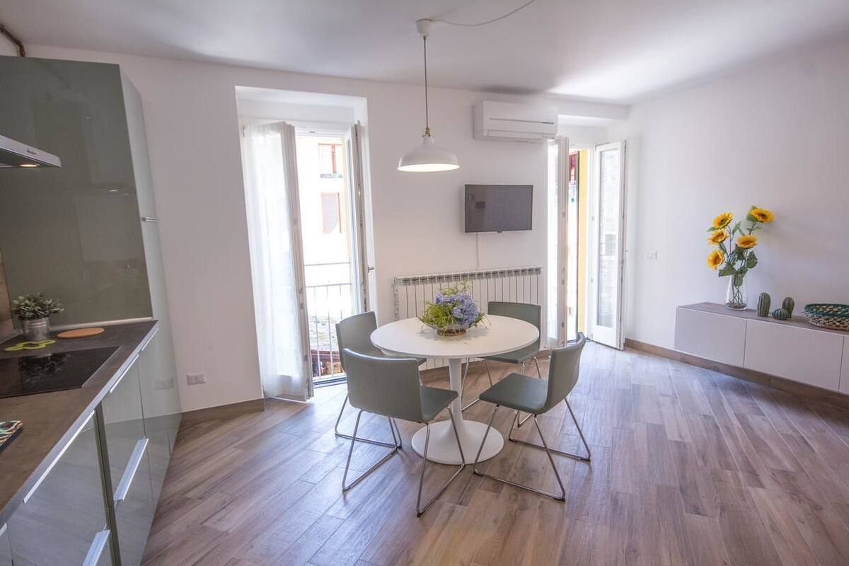 Una cocina moderna con estufa integrada, un comedor con una mesa redonda y cuatro sillas, y un amplio ventanal que proporciona luz natural.