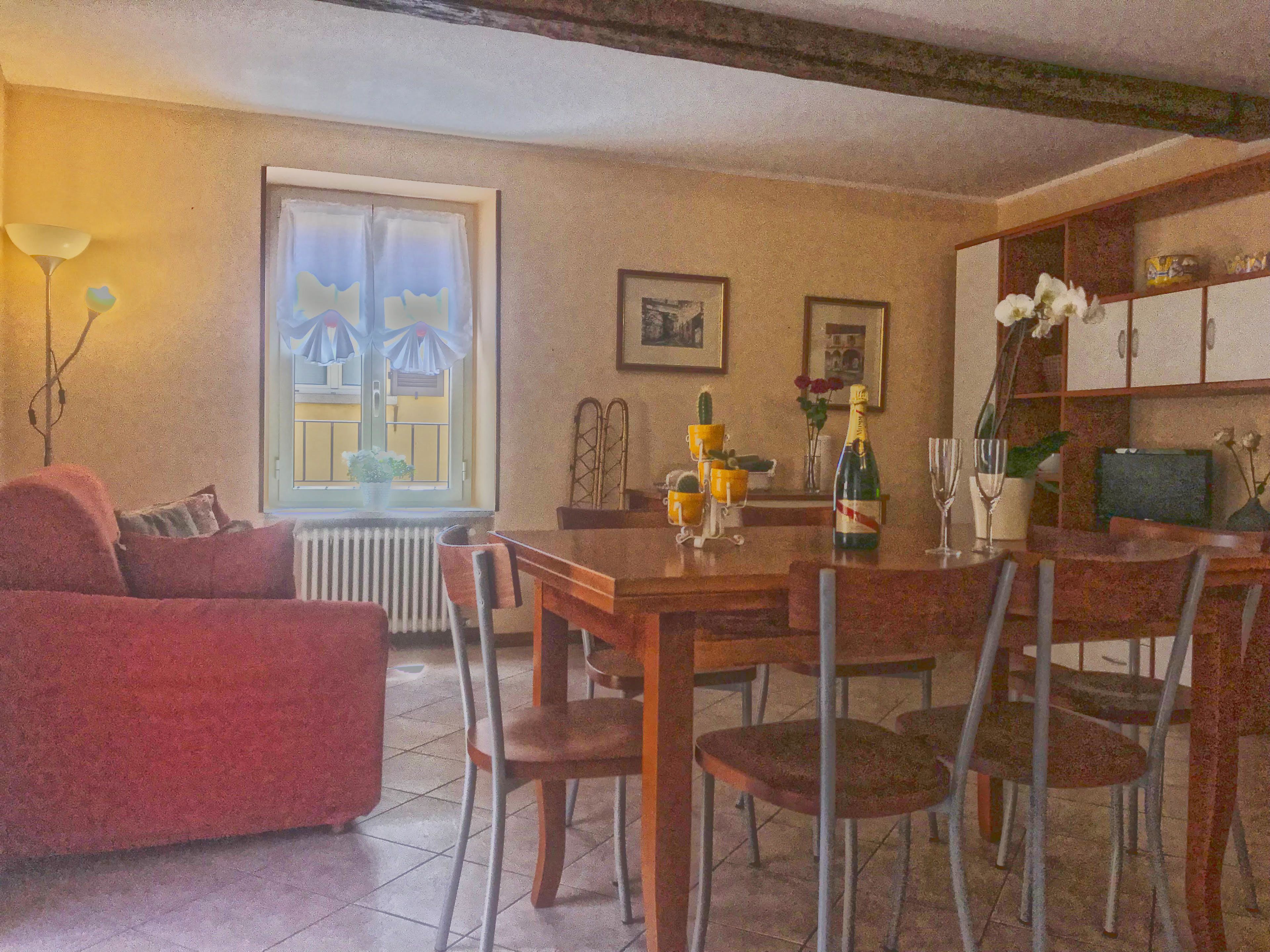 Un coin repas comprenant une table en bois, des chaises, un canapé rouge, une fenêtre avec des rideaux et une bibliothèque contenant divers objets.