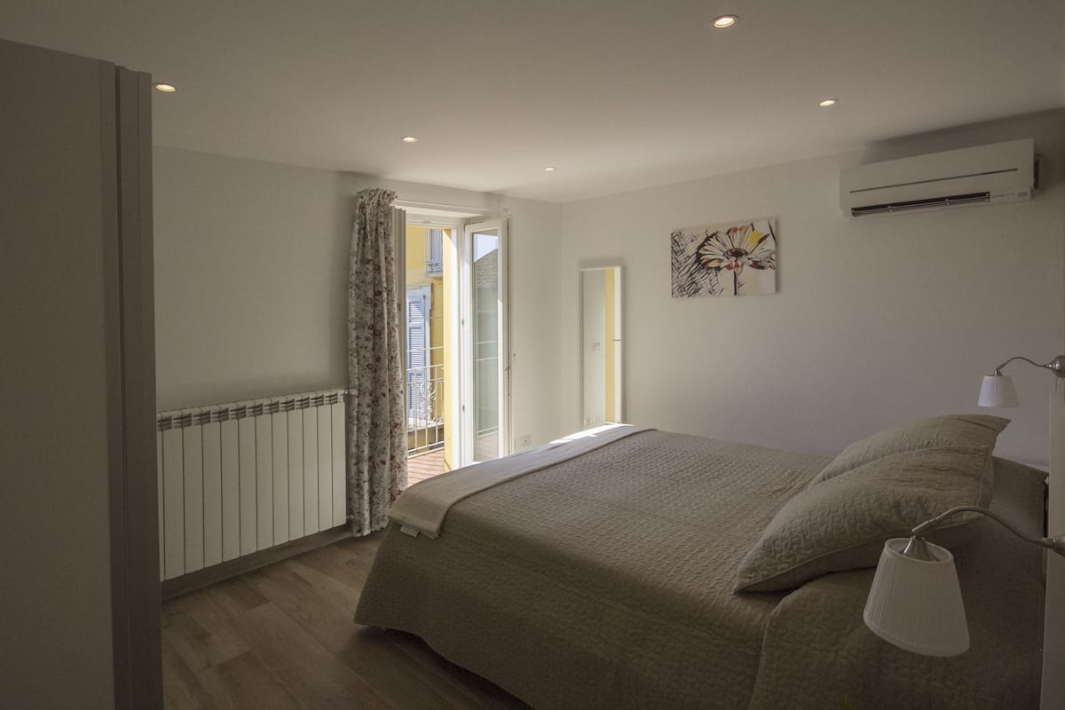 Un dormitorio con cama, mesita de noche, lámpara y ventana con cortinas.