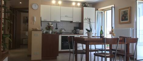 Une cuisine spacieuse avec des meubles blancs, un coin repas doté de chaises en bois et une grande fenêtre qui laisse entrer la lumière naturelle.