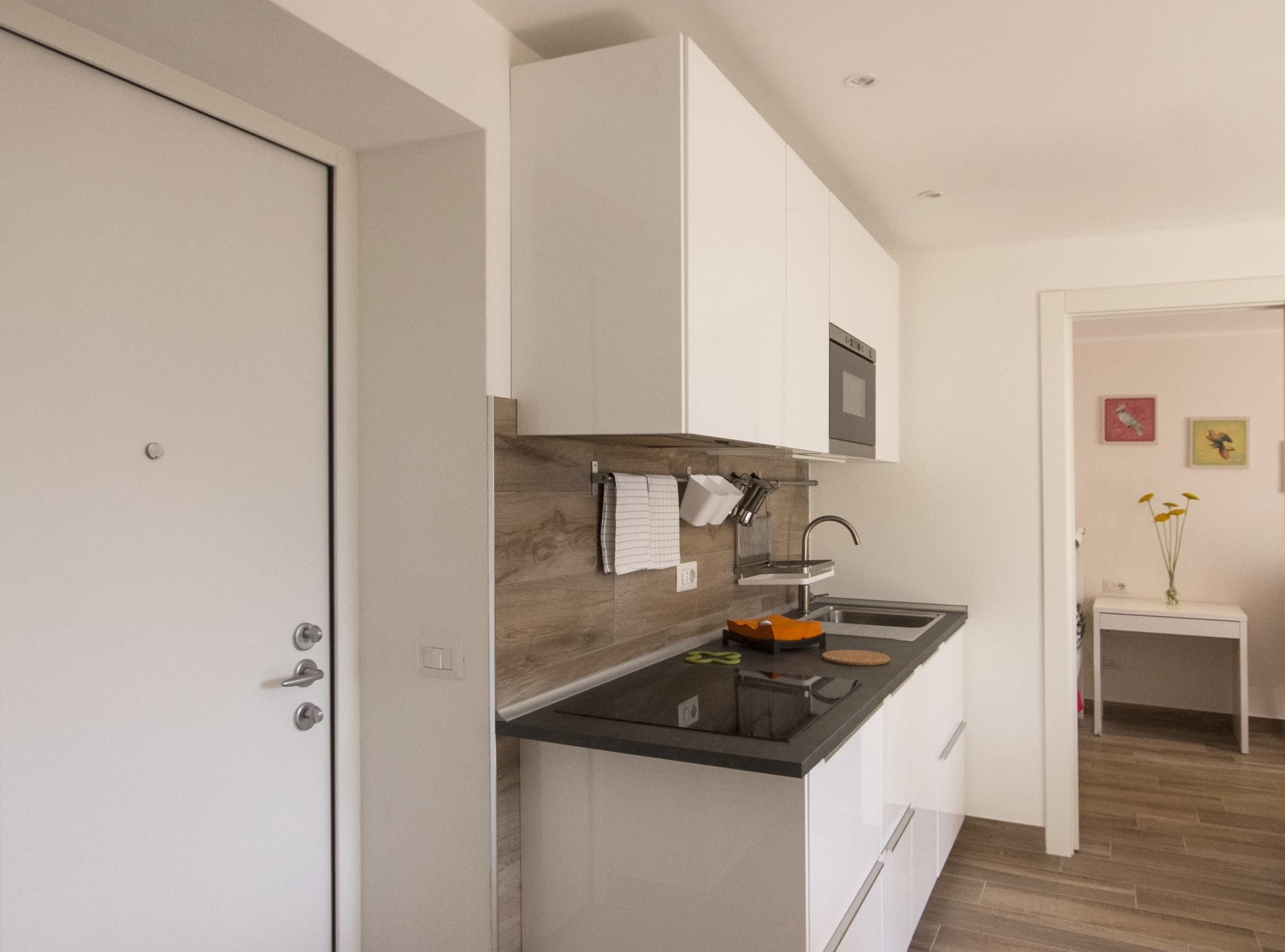 Cozinha moderna com armários brancos, bancada preta e painel de madeira.