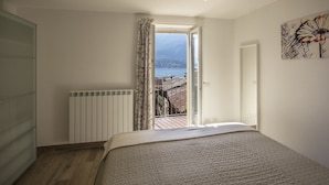 Une chambre à coucher avec un lit, un radiateur, une fenêtre avec des rideaux et une vue sur une étendue d’eau et des bâtiments.