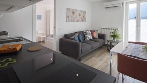 Une cuisine moderne avec un plan de travail noir, un coin repas avec une chaise rouge, un canapé gris agrémenté de coussins décoratifs et une vue sur l’extérieur grâce à une grande fenêtre.
