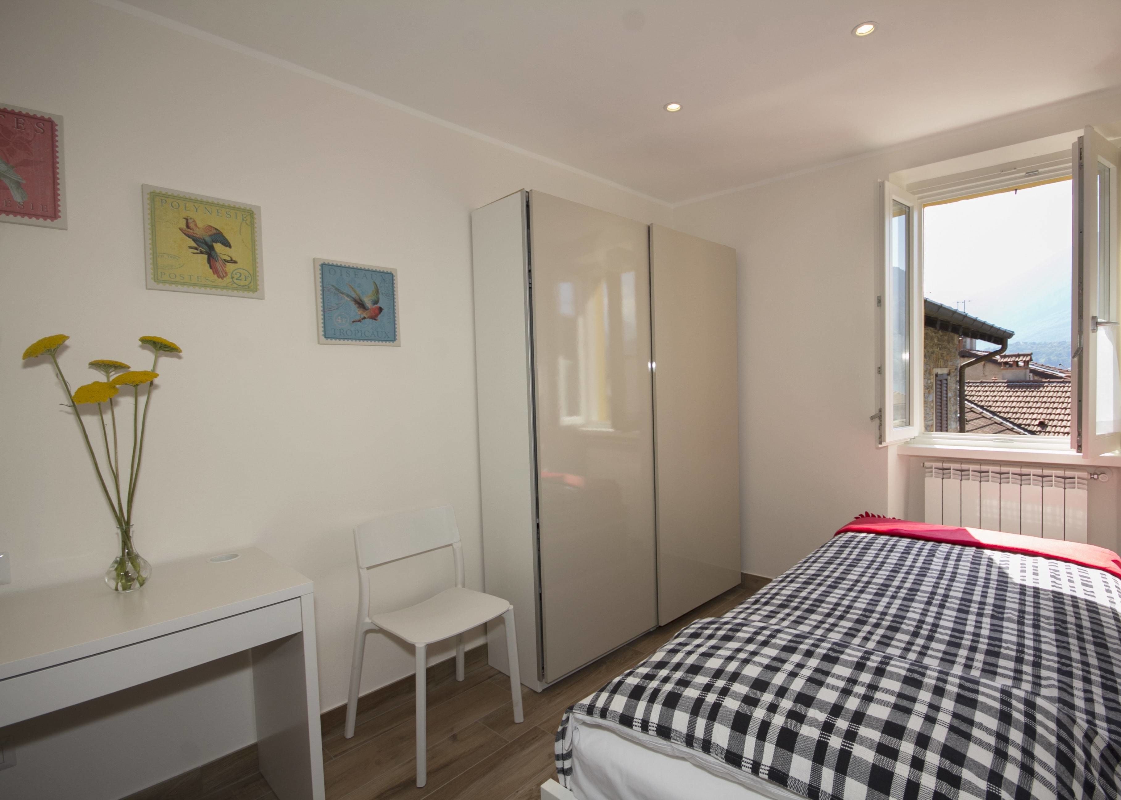 A bedroom with a bed, a desk, a chair, and a window with a view of buildings.