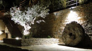 A stone wall with a large rock and a tree illuminated by artificial lighting. - Suites in Erbalunga (Brando)