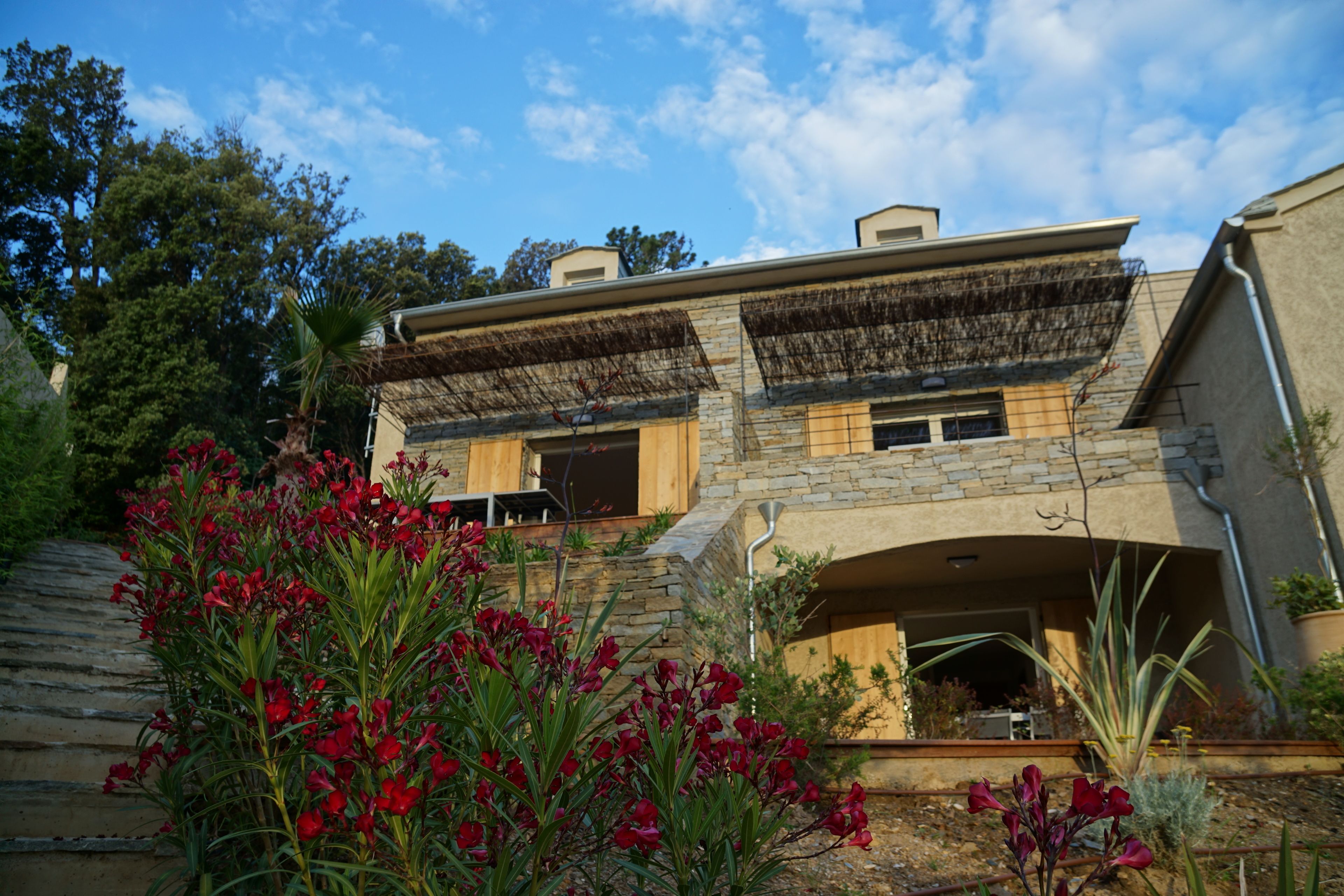Une maison en pierre à deux étages, dotée d’un toit plat et d’un patio couvert.