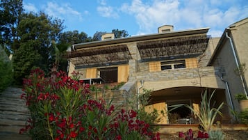 Une maison en pierre à deux étages, dotée d’un toit plat et d’un patio couvert.