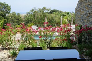 Un área junto a la piscina con un muro de piedra, asientos al aire libre y flores rosadas floreciendo.
