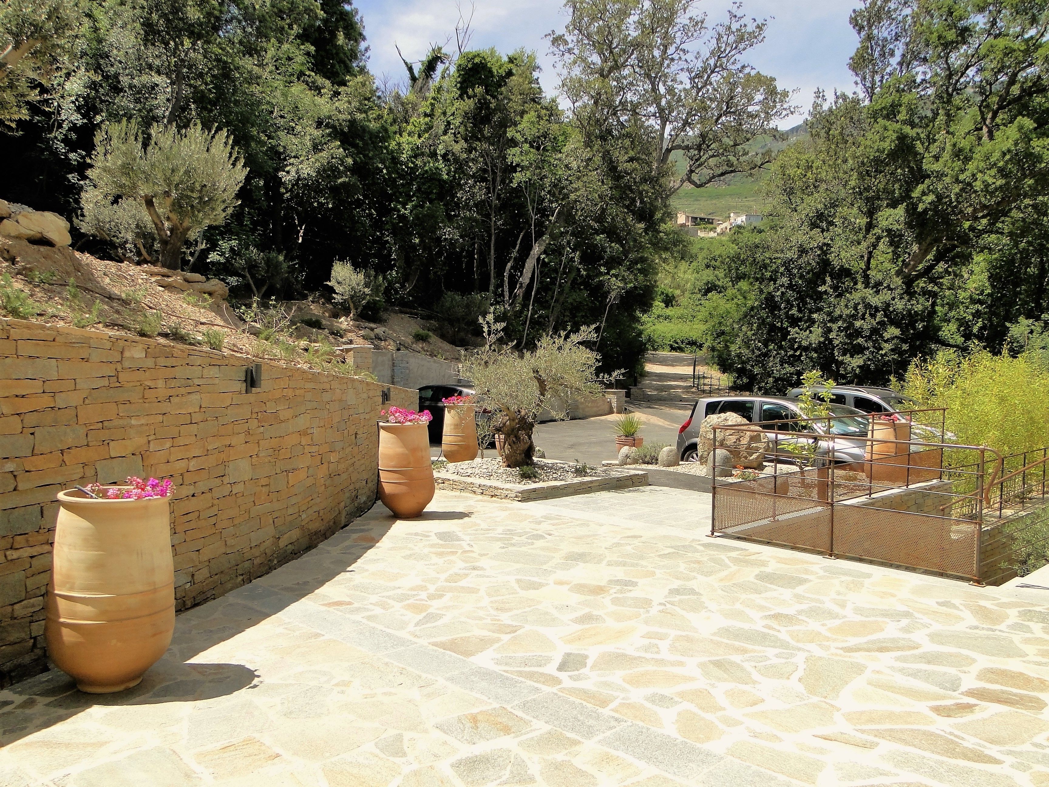 A paved pathway leading to a parking area with stone walls and large planters.
