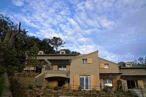 Una casa moderna de dos pisos con muros de piedra y contraventanas de madera, que cuenta con una escalera de piedra y vistas del paisaje circundante.