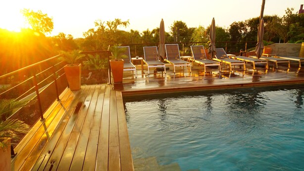 A wooden deck with lounge chairs and umbrellas, overlooking a swimming pool. - Suites in Erbalunga (Brando)