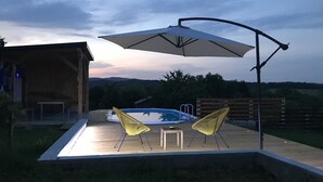 Une terrasse extérieure avec un jacuzzi, deux chaises jaunes et un parasol.