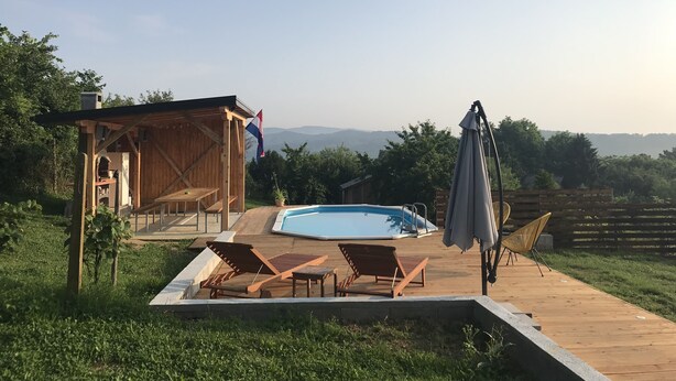 Une terrasse en bois avec une piscine, des chaises longues et un espace abrité orné d’un drapeau.