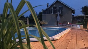 Une terrasse en bois avec une piscine, une maison dotée d’un balcon et une chaise.
