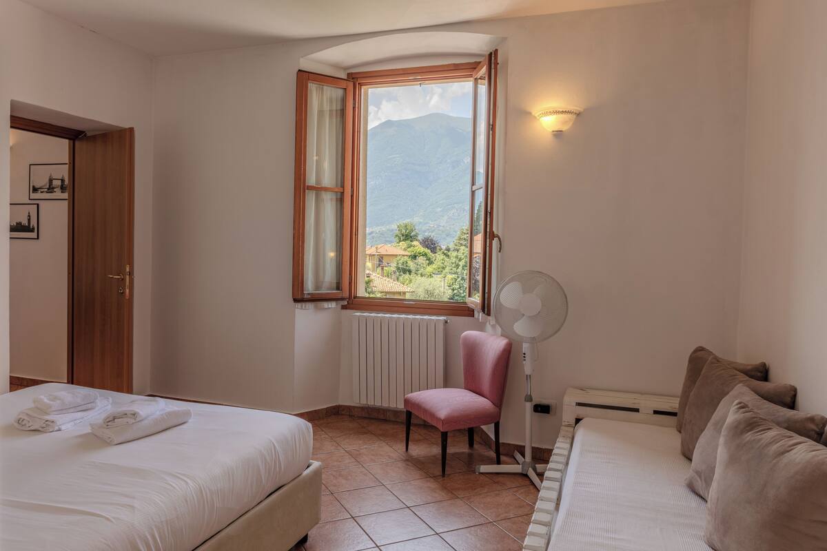 A bedroom with two beds, a window with a mountain view, a standing fan, and a radiator.