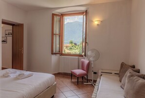Egy hálószoba két ággyal, egy ablakkal, amelyből hegyre nyílik a kilátás, egy állóventilátorral és egy radiátorral.