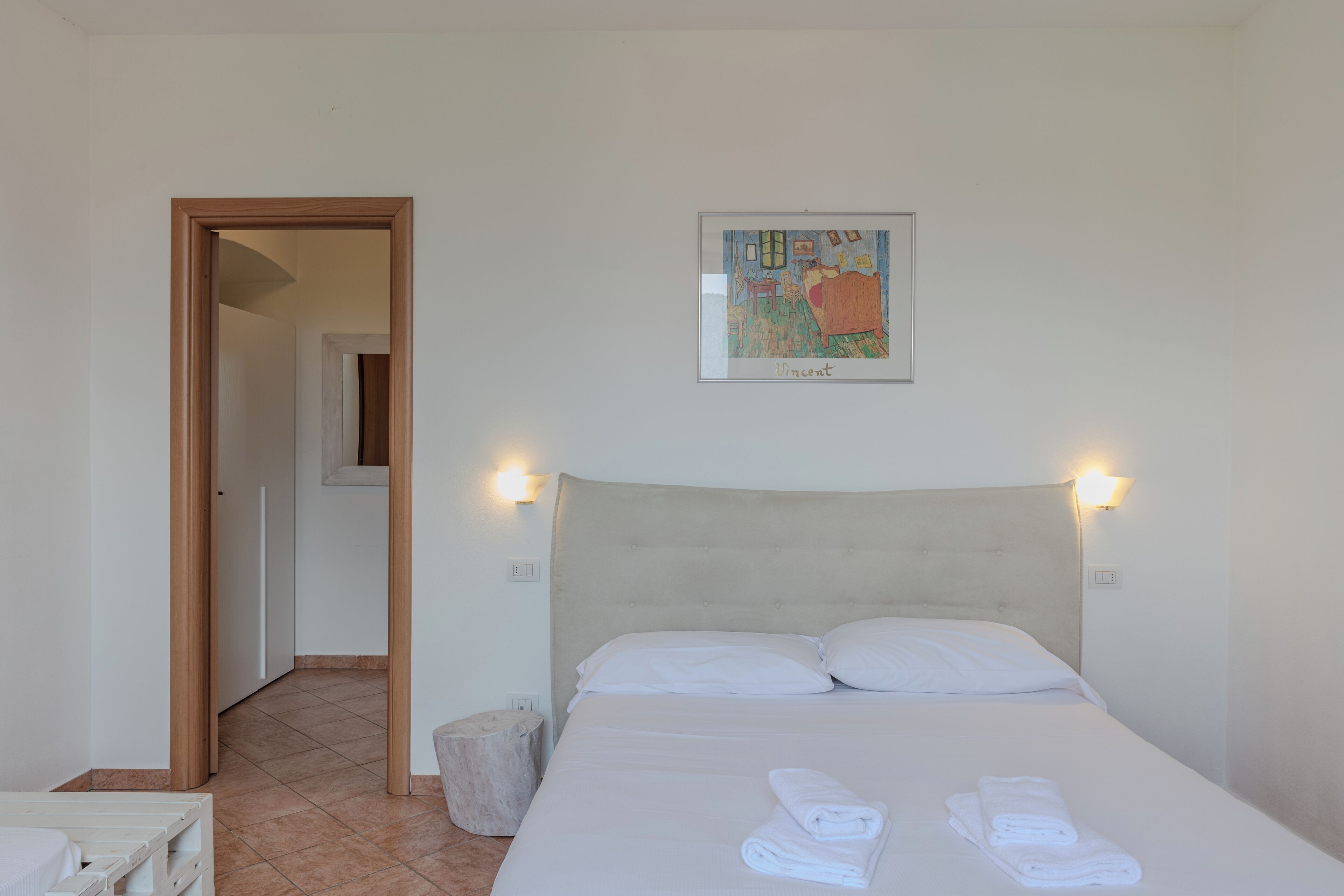 Een hotelkamer met een bed, een lijst met kunstwerk aan de muur en een deur die naar een andere kamer leidt.