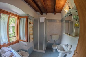 Baño con ducha, inodoro, lavabo y ventana con cortinas.