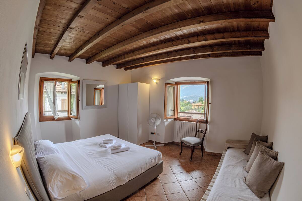 A bedroom with a bed, a chair, a sofa, a window with a view, and a wooden ceiling.