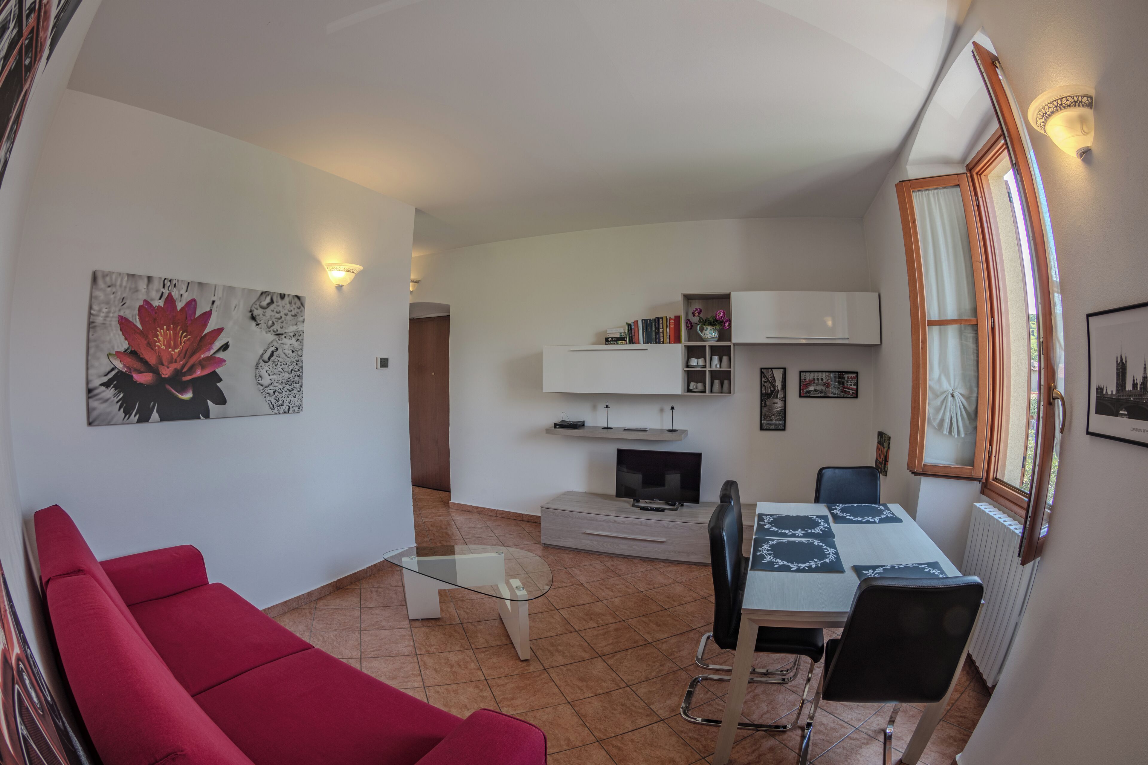 Un espace de vie compact comprenant un canapé rouge, une table basse en verre, une table à manger avec des chaises, un téléviseur et une bibliothèque.