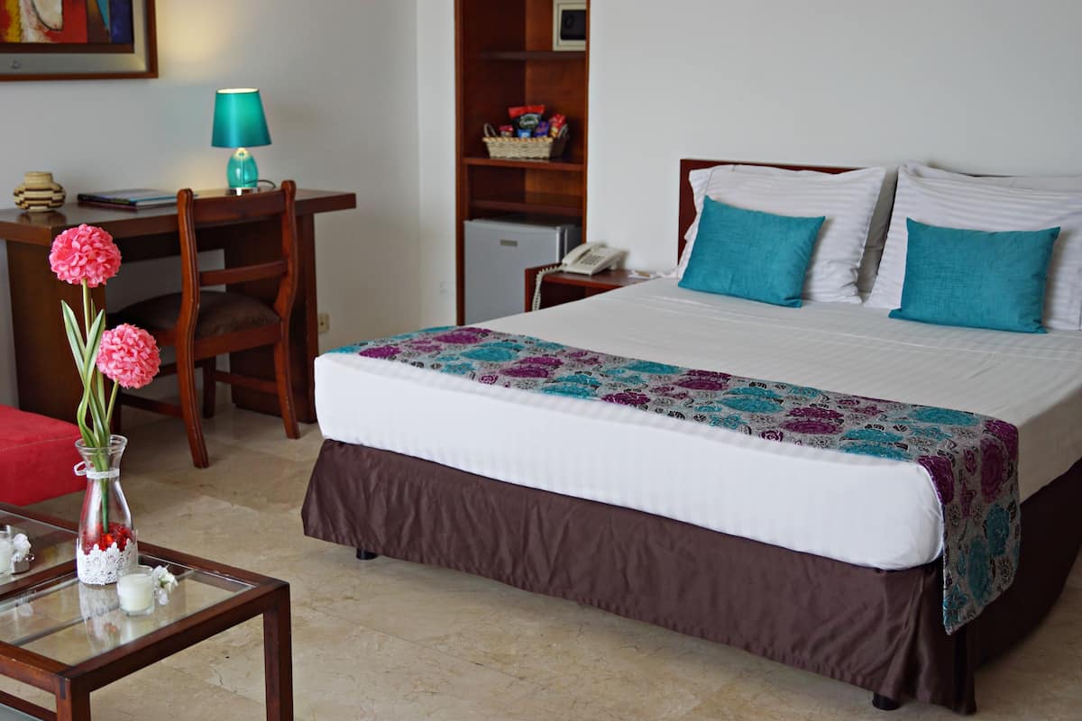 A hotel room with a bed, a desk, a chair, a lamp, and a vase with flowers.