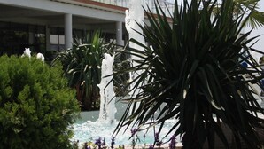 A modern building with multiple balconies and a central fountain surrounded by greenery.