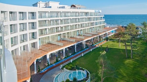 A modern hotel with multiple balconies, a pool area, and a view of the sea.