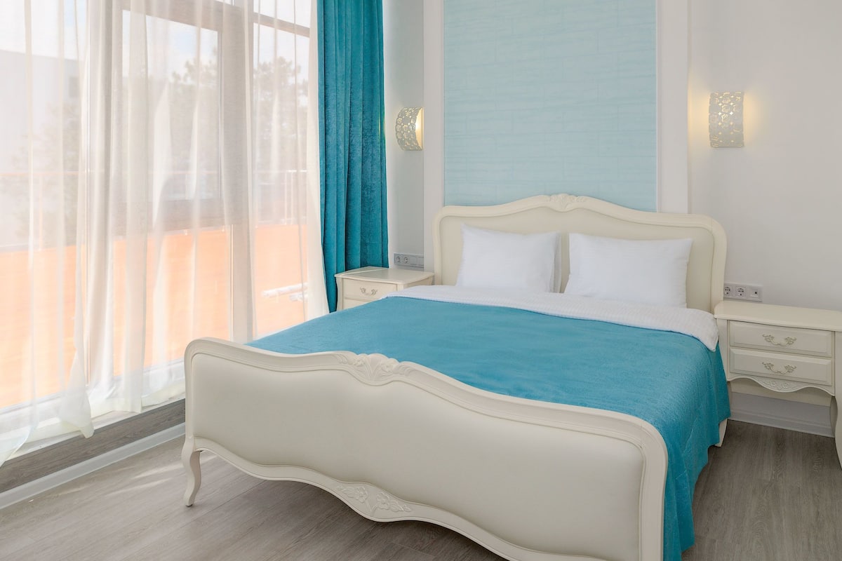 A neatly arranged bedroom with a bed, bedside tables, and a window with curtains.