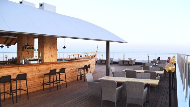 A wooden deck with a bar area, wicker furniture, and a view of the sea.