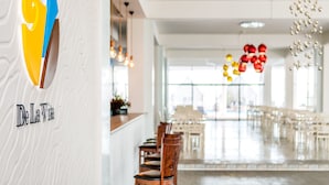 A modern dining area with a white textured wall, a logo, and a view of the dining space with tables and chairs.