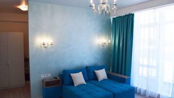 A modern living room with a blue sofa, a chandelier, and a large window with curtains.